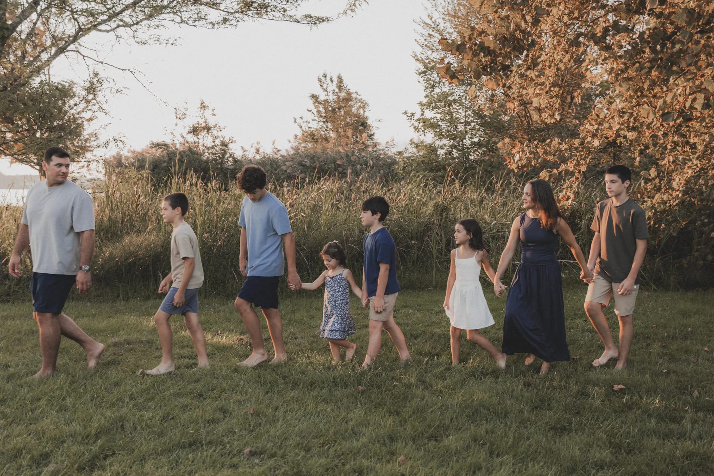 A big family walking across a sunlit lawn by the water