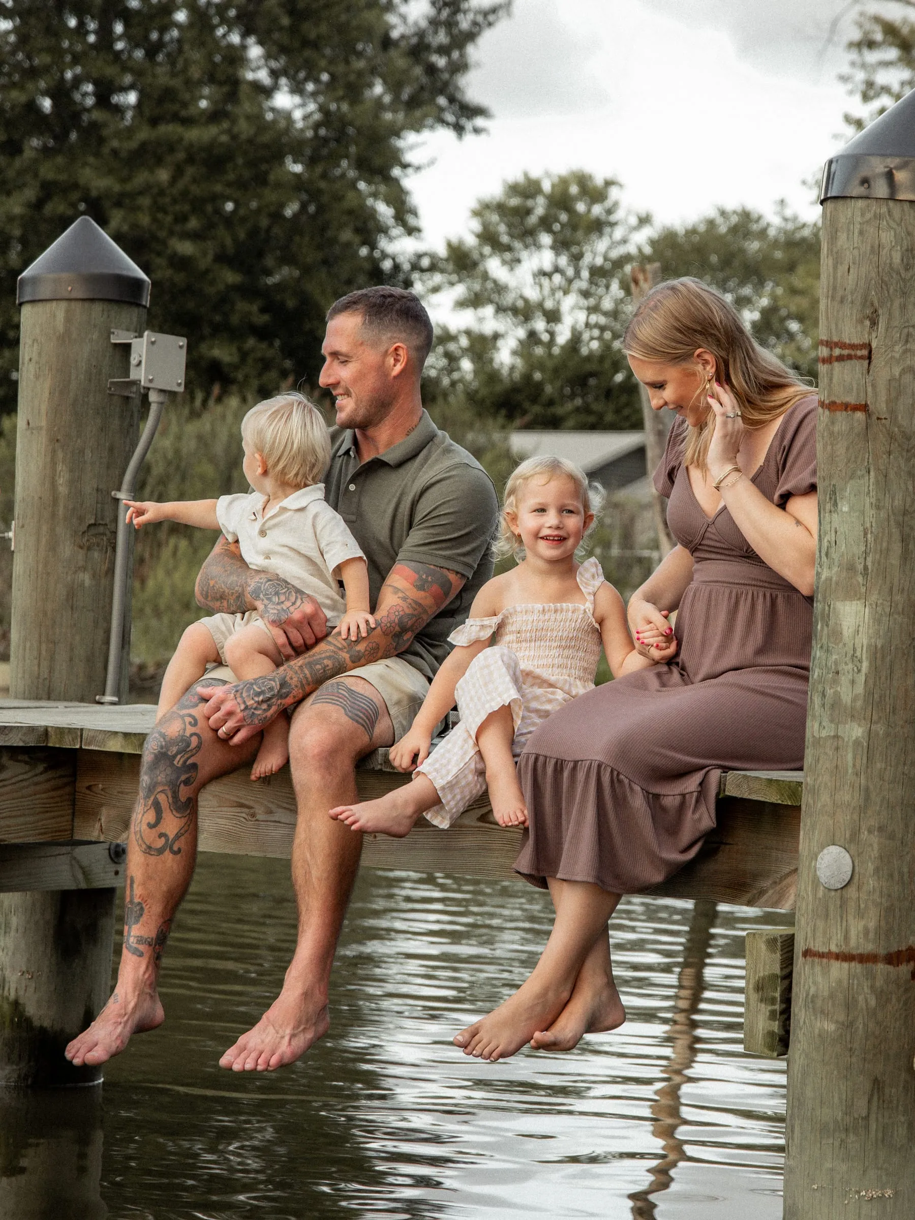 A laughing family of four sitting on a dock with their feet dangling over the water