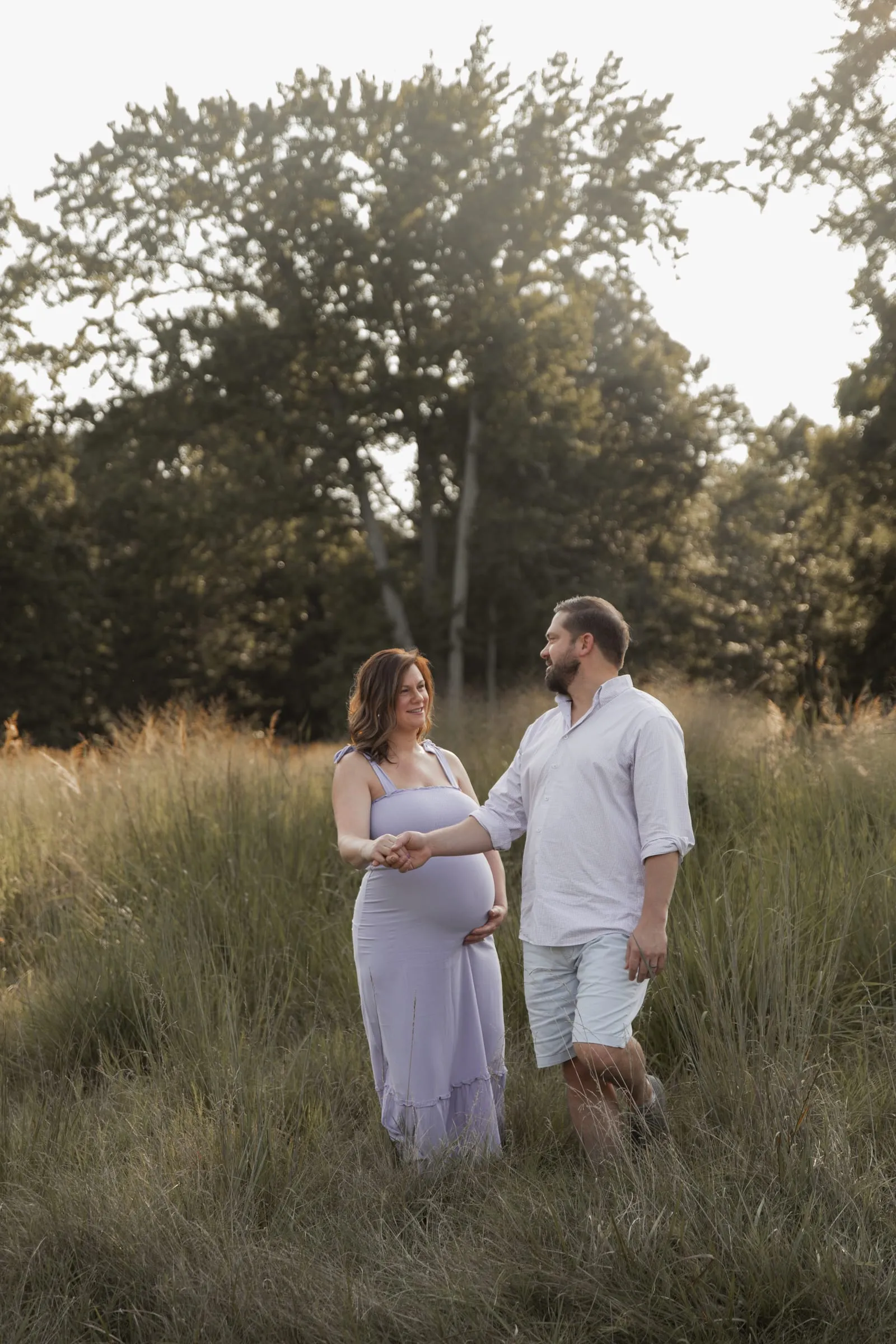 A husband leading his expecting wife by the hand through tall golden grass
