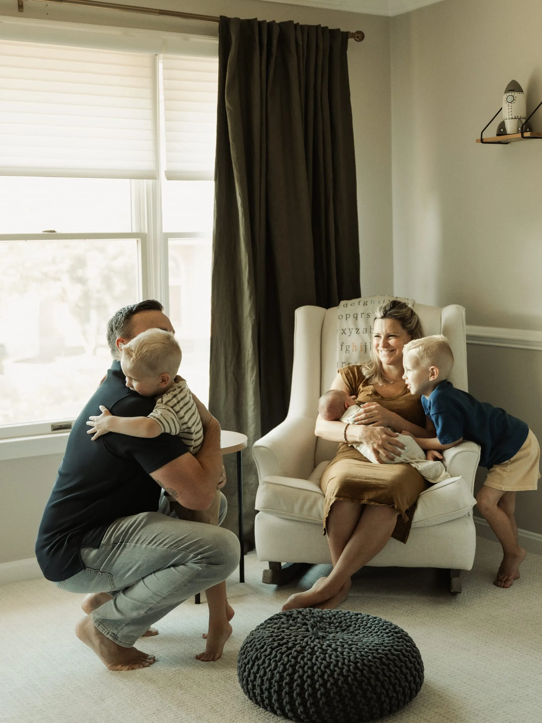 A family of five gathered around mom and the new baby in a nursery rocking chair