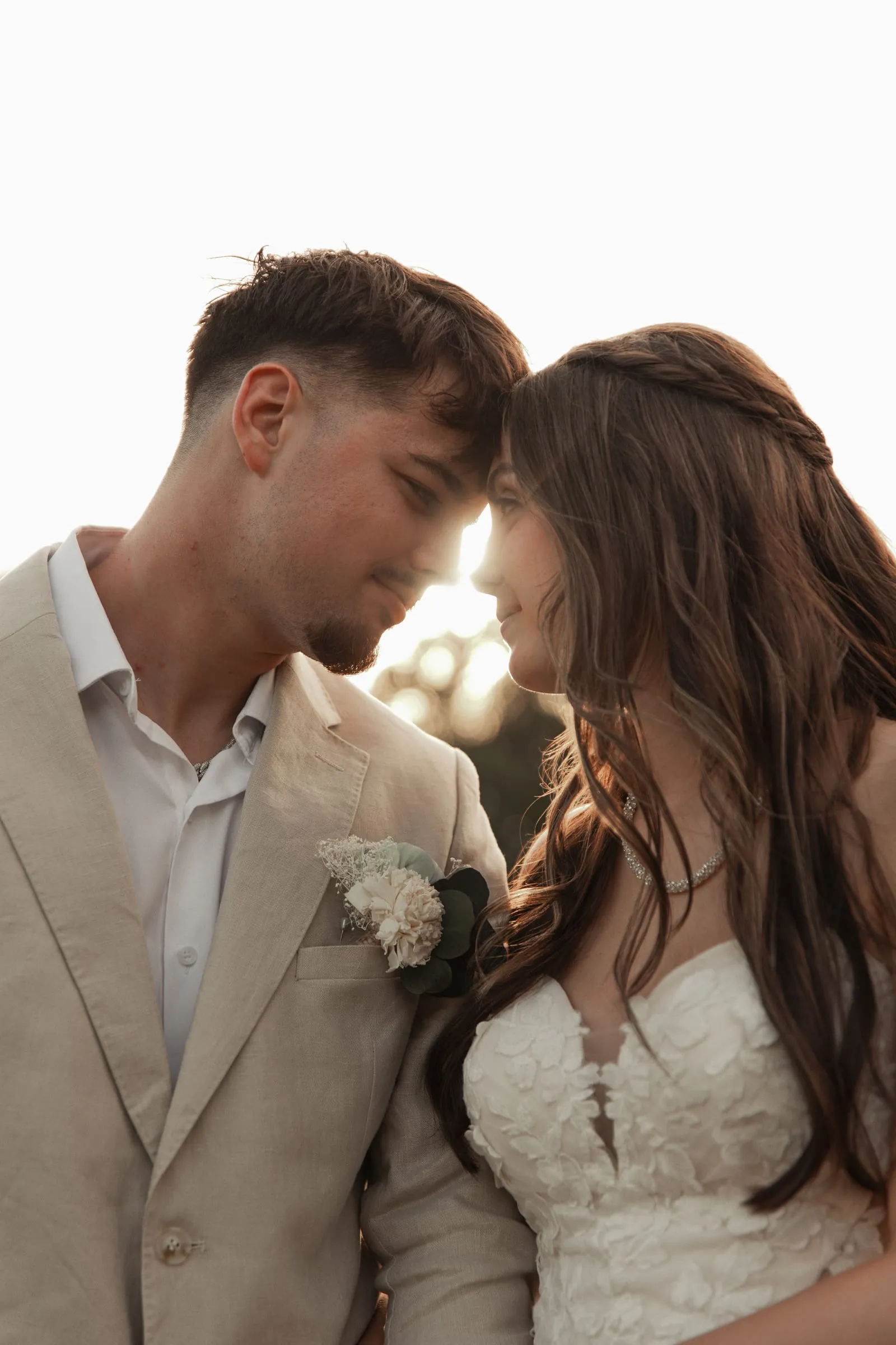 Bride and groom touching foreheads in glowing golden-hour light
